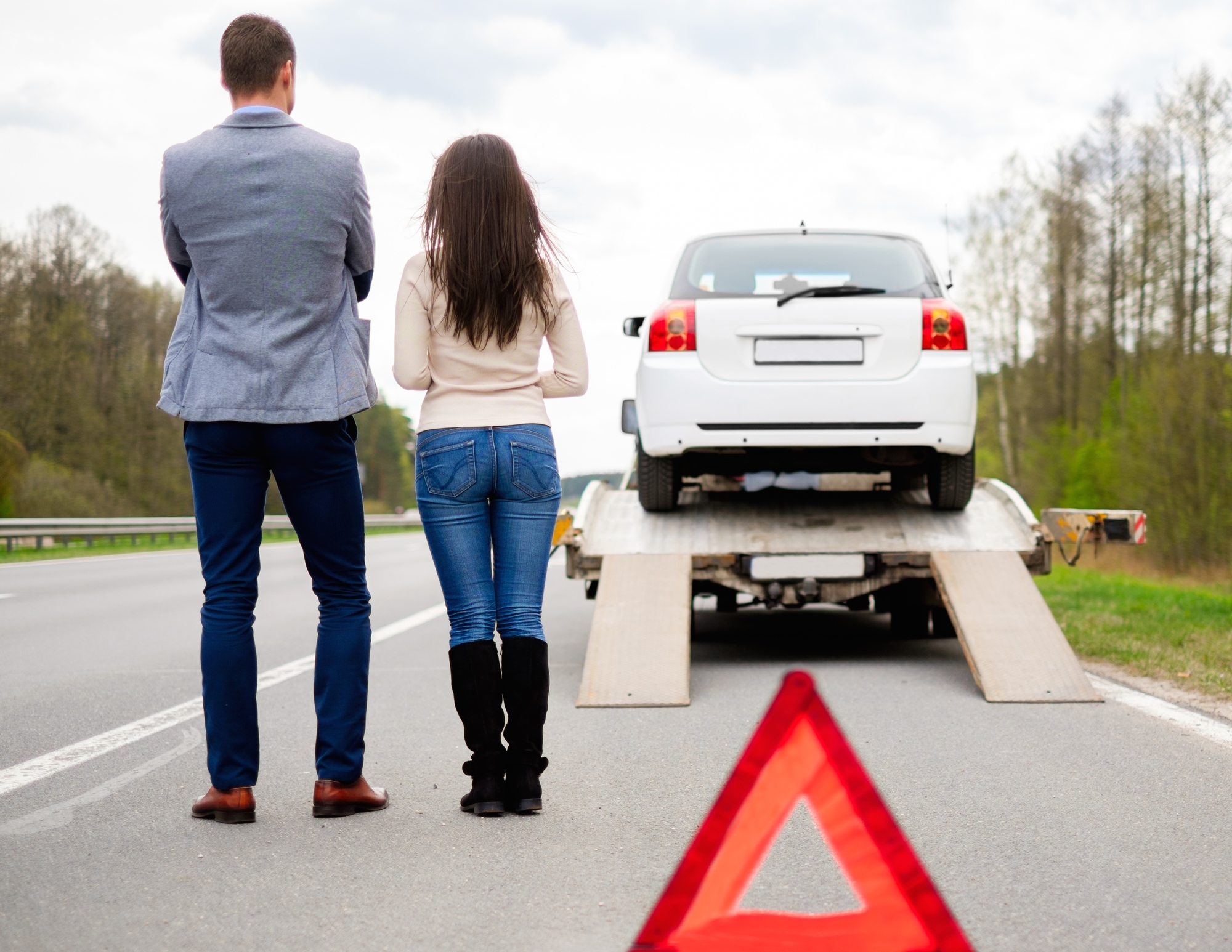 A man and woman standing next to a tow truck.