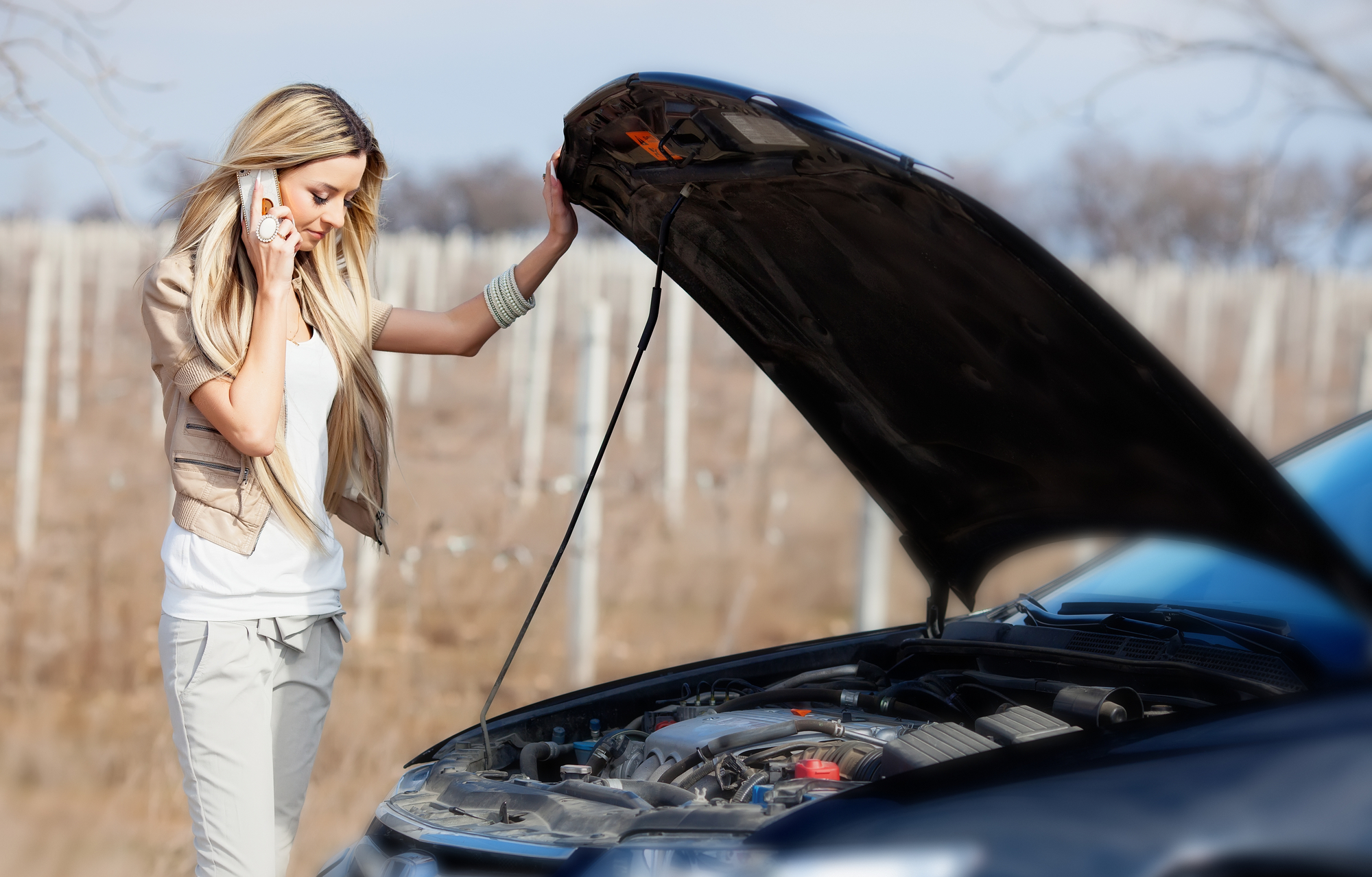 A woman talking on a cell phone while standing next to a broken car.